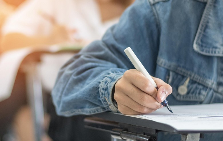 Schüler sitzt mit blauer jeans Jacke am Tisch und schreibt eine Prüfung