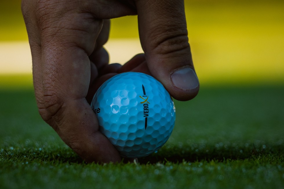 Hand hält Golfball direkt über den grünen Rasen